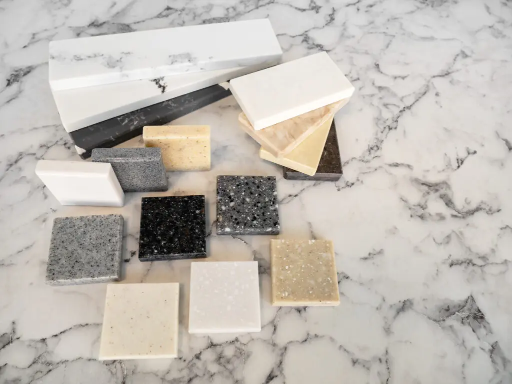 Various quartz and marble countertop samples in different colors and patterns, displayed on a marble surface, showcasing options for kitchen renovation