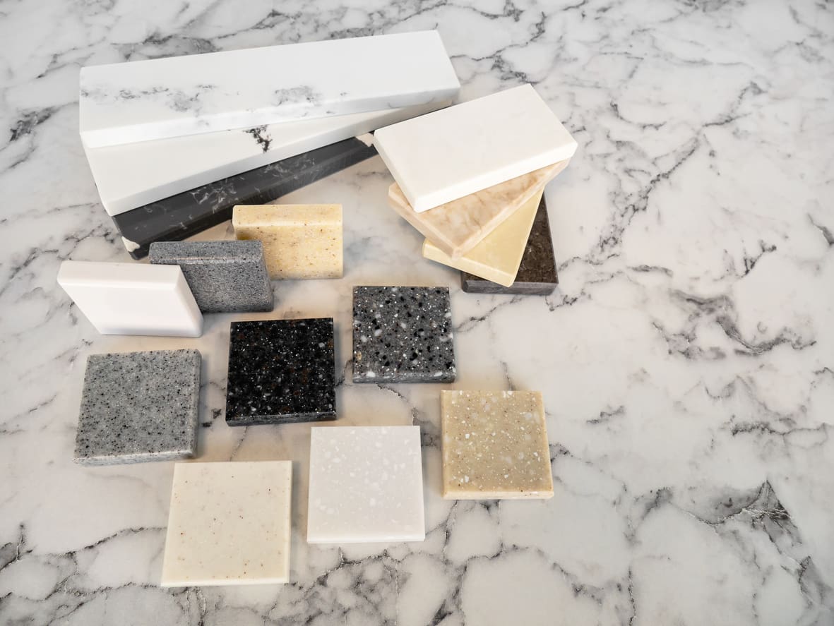 Various quartz and marble countertop samples in different colors and patterns, displayed on a marble surface, showcasing options for kitchen renovation