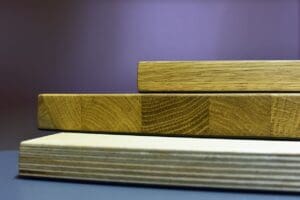 Three wooden boards stacked in a staggered manner against a blurred, dark background, reminiscent of the choices you'll encounter when learning how to choose kitchen cabinets. The boards display various shades and grain patterns, highlighting their natural textures.
