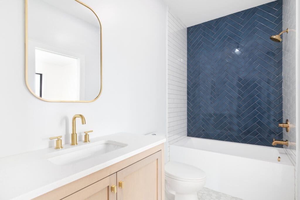 Step 4 of the 7 Bathroom Remodeling steps: A modern bathroom with a blue herringbone tile accent wall, gold fixtures, and a white vanity showcasing a stylish and functional design.