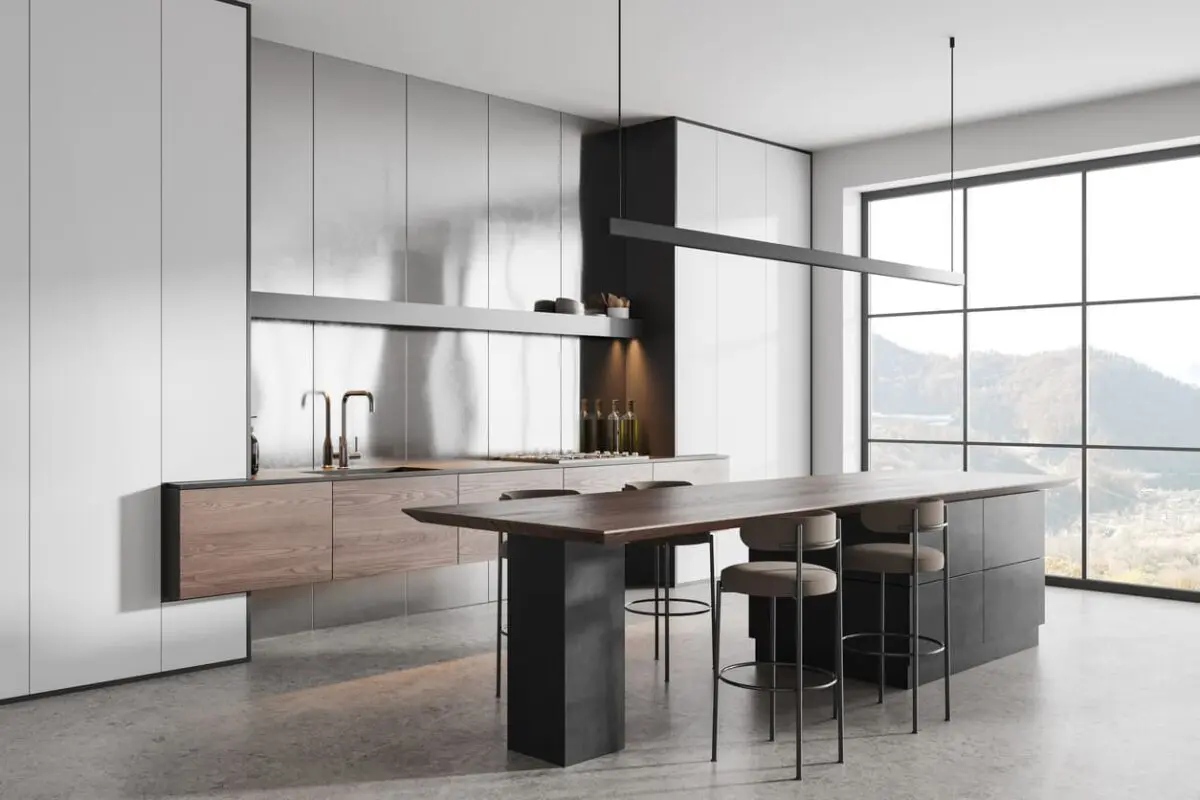 Minimalist kitchen featuring floating wooden cabinets paired with sleek white and metallic wall cabinetry. A large wooden dining table with black pedestal legs anchors the space, complemented by industrial-style bar stools and large floor-to-ceiling windows showcasing scenic outdoor views