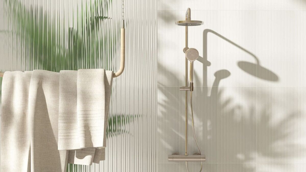 Bathroom shower featuring stacked vertical white tiles, a gold rain shower head, and a beige towel hanging nearby, with soft natural light casting plant shadows on the wall.