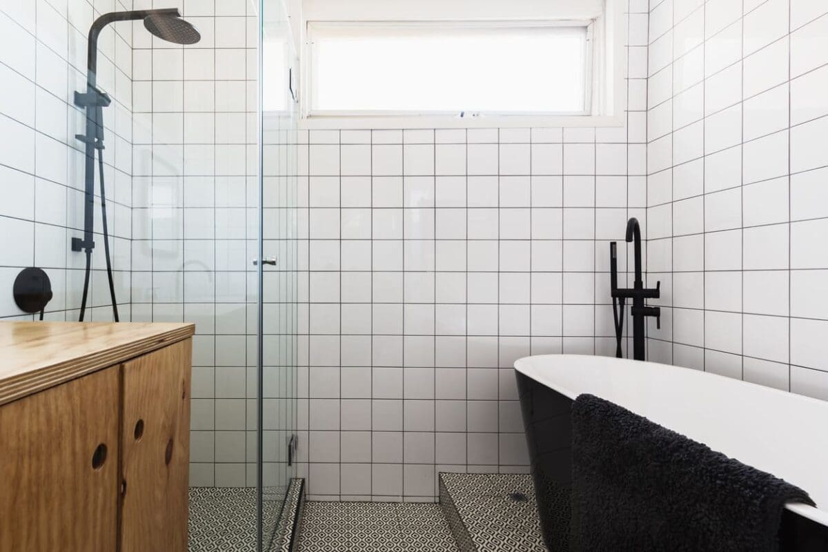 Bathroom with classic white brick bond (offset) tile layout on walls, black fixtures including a rain shower head and freestanding tub faucet, geometric patterned floor tiles, a wooden vanity, and a black freestanding bathtub. A timeless and stylish design.
