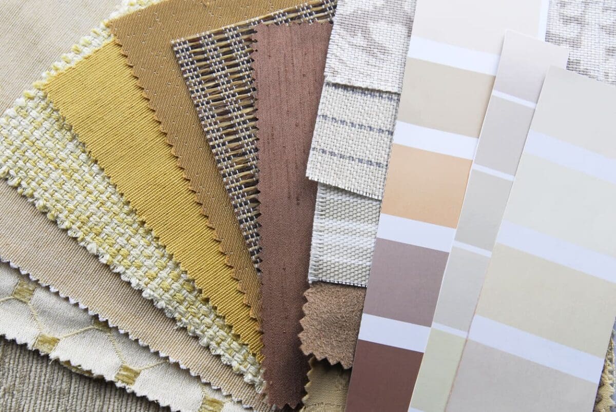 A collection of fabric swatches in neutral tones, such as beige, brown, and cream, displayed alongside a series of paint color strips. The swatches have various textures and patterns, and the paint strips feature complementary shades.
