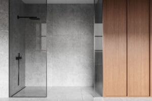 Minimalist bathroom featuring a walk-in shower with gray stone walls and floor, black shower fixtures, and a glass partition next to light wooden cabinets.