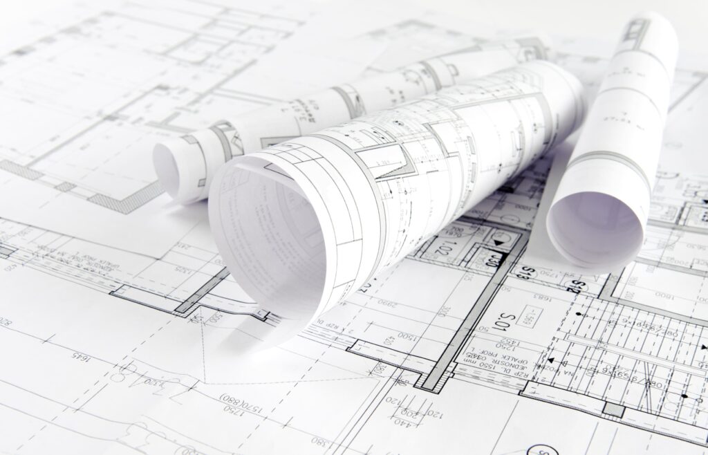Three rolled-up blueprints rest on unrolled architectural floor plans, displaying technical drawings, measurements, and construction details for a Commercial Renovation in NYC.
