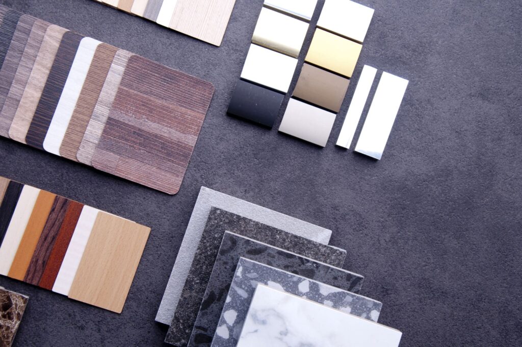 Samples of laminate wood, metal, stone, and engineered quartz countertops are arranged neatly on a dark grey surface, showcasing various colors and textures for interior design selection.