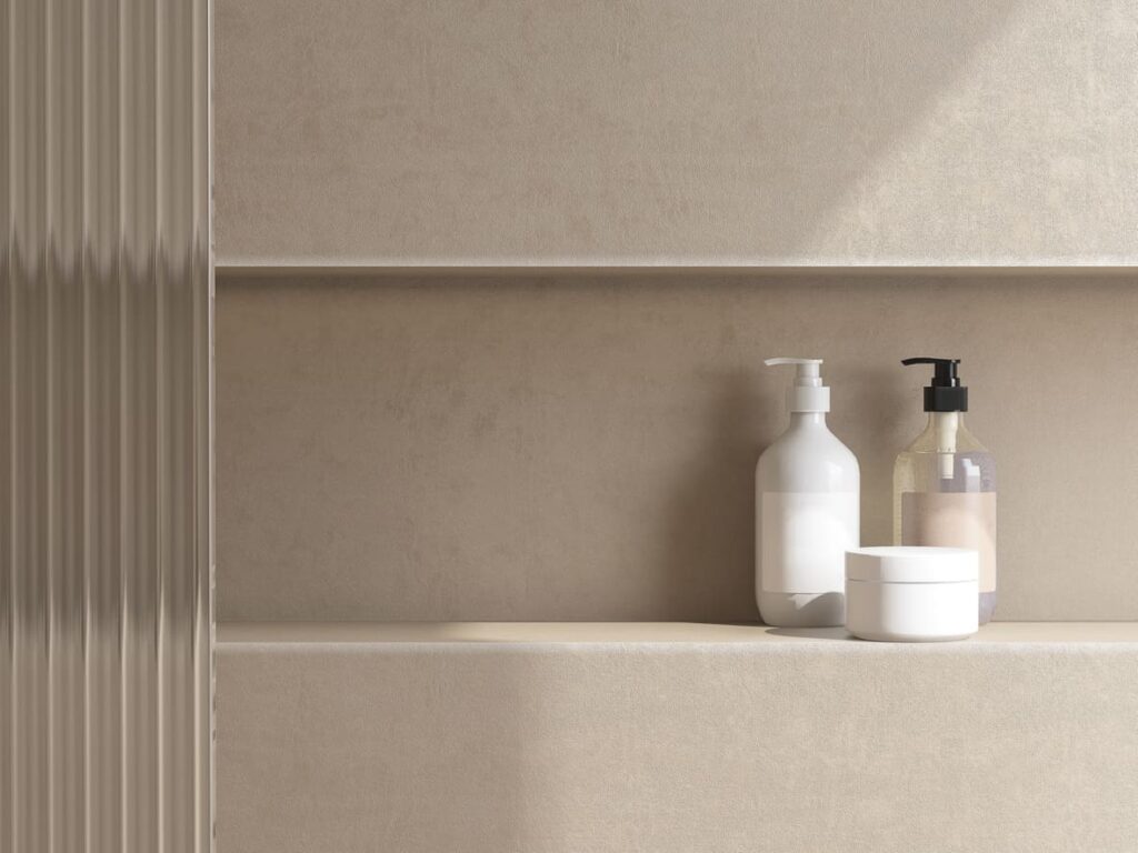 Minimalist bathroom shelf with three items: a white pump bottle, a clear bottle with a black pump, and a white round container, all set against a beige textured wall with soft natural lighting.