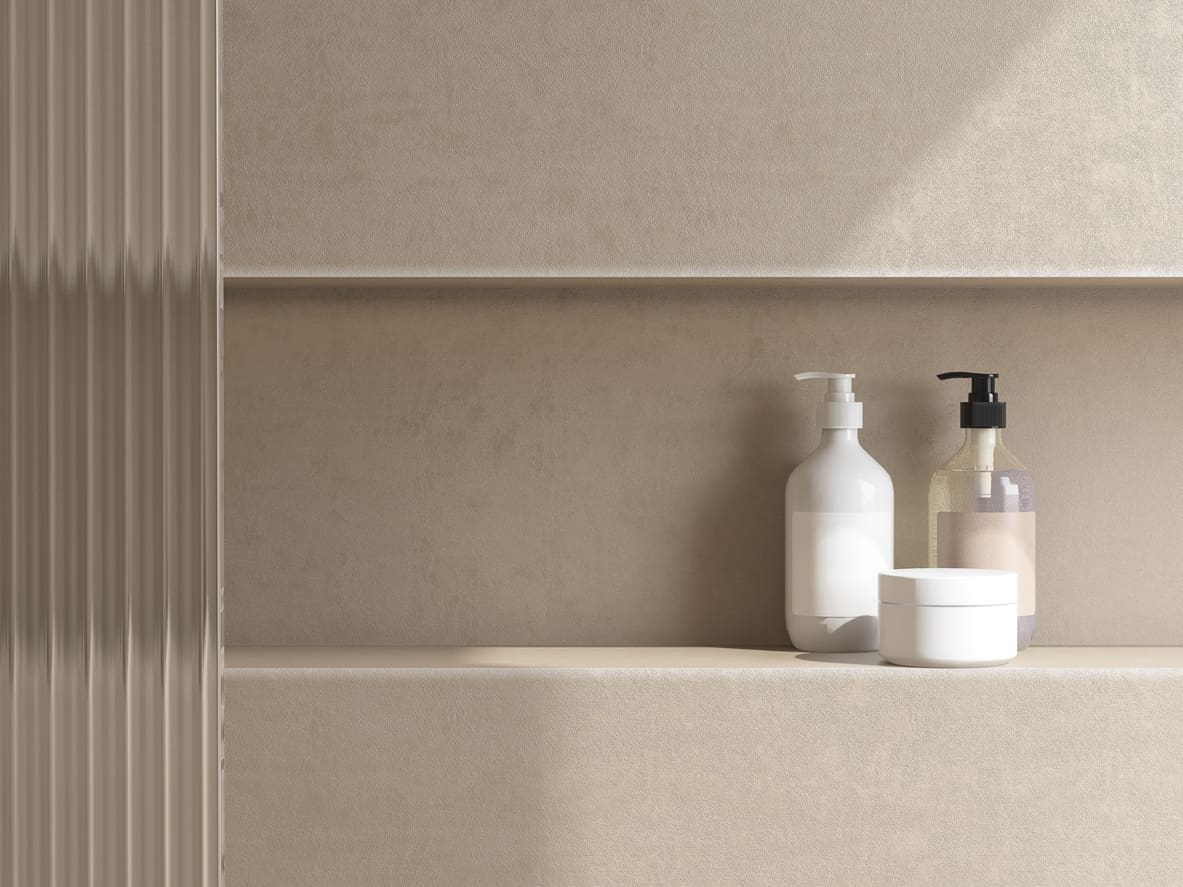 Minimalist bathroom shelf with three items:  Single Niche, a white pump bottle, a clear bottle with a black pump, and a white round container, all set against a beige textured wall with soft natural lighting.