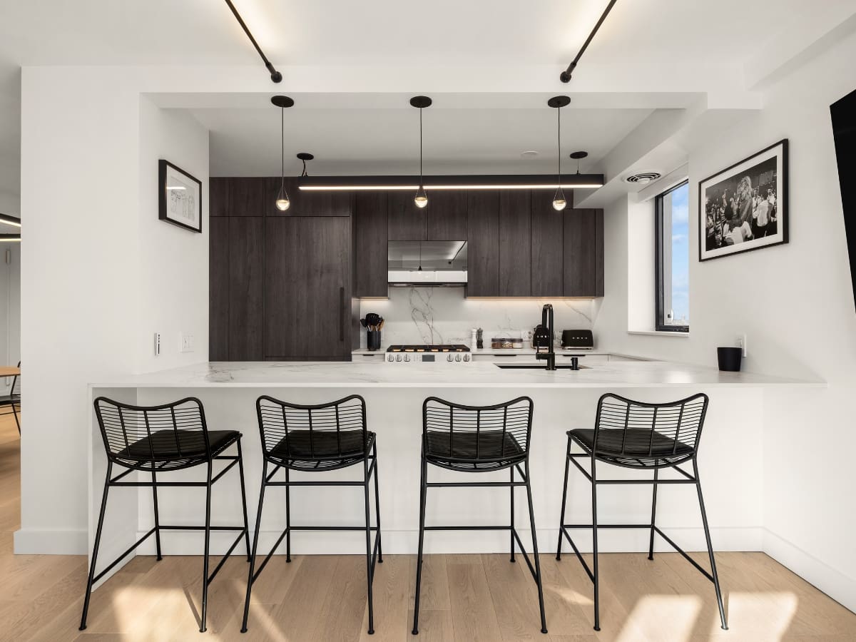 Open galley kitchen remodel in NYC apartment with white peninsula seating, dark wood cabinets, marble backsplash, and modern lighting
