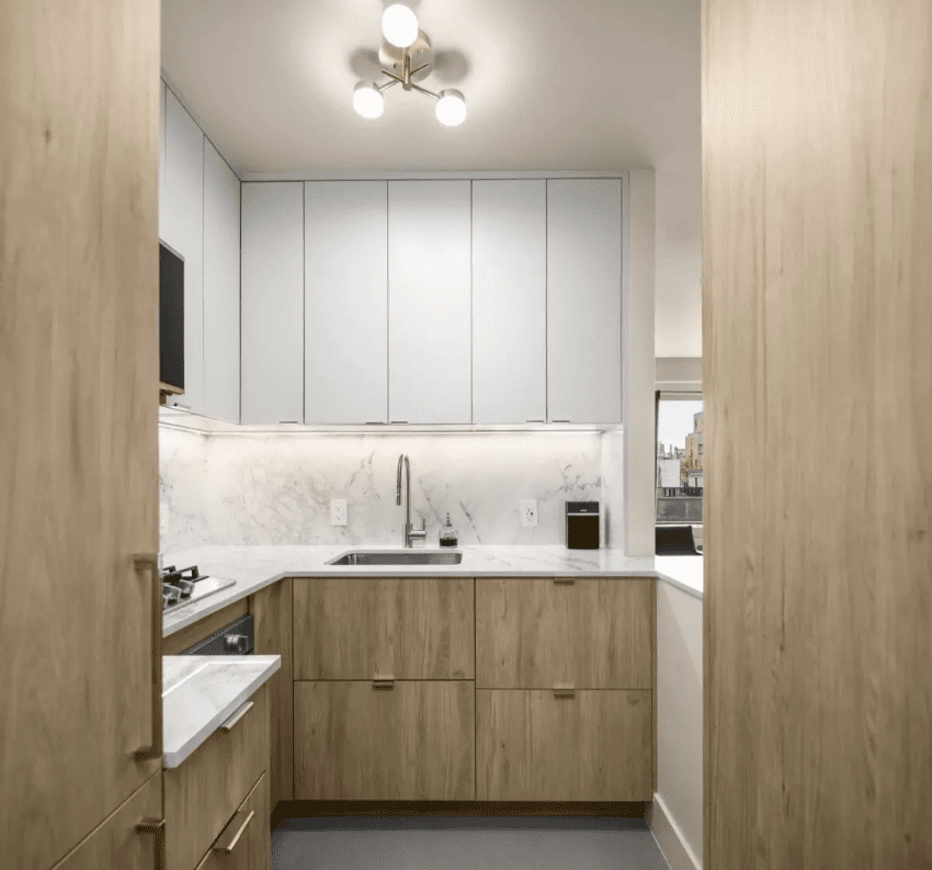 Modern kitchen renovation favorite with light wood cabinets, white marble countertops and backsplash, under-cabinet lighting, built-in appliances, and a sleek overhead light fixture.