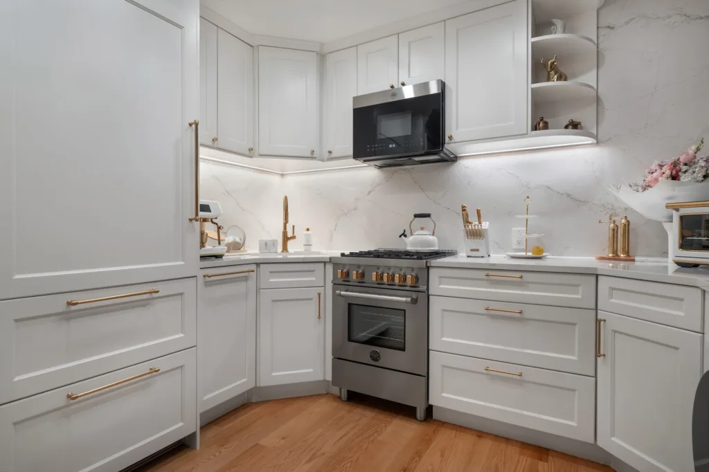 White kitchen cabinets, brass hardware, and stainless steel range in a renovated Upper West Side apartment