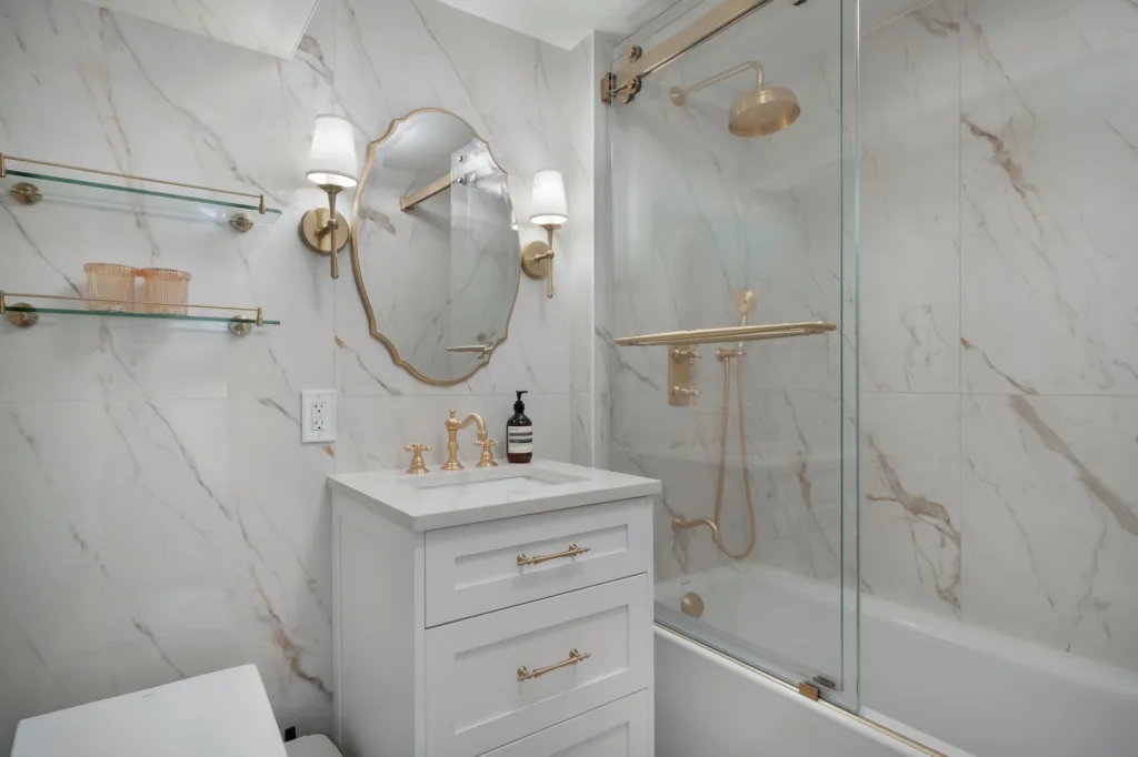 Upper West Side bathroom renovation with white vanity, brass fixtures, and glass shower screen