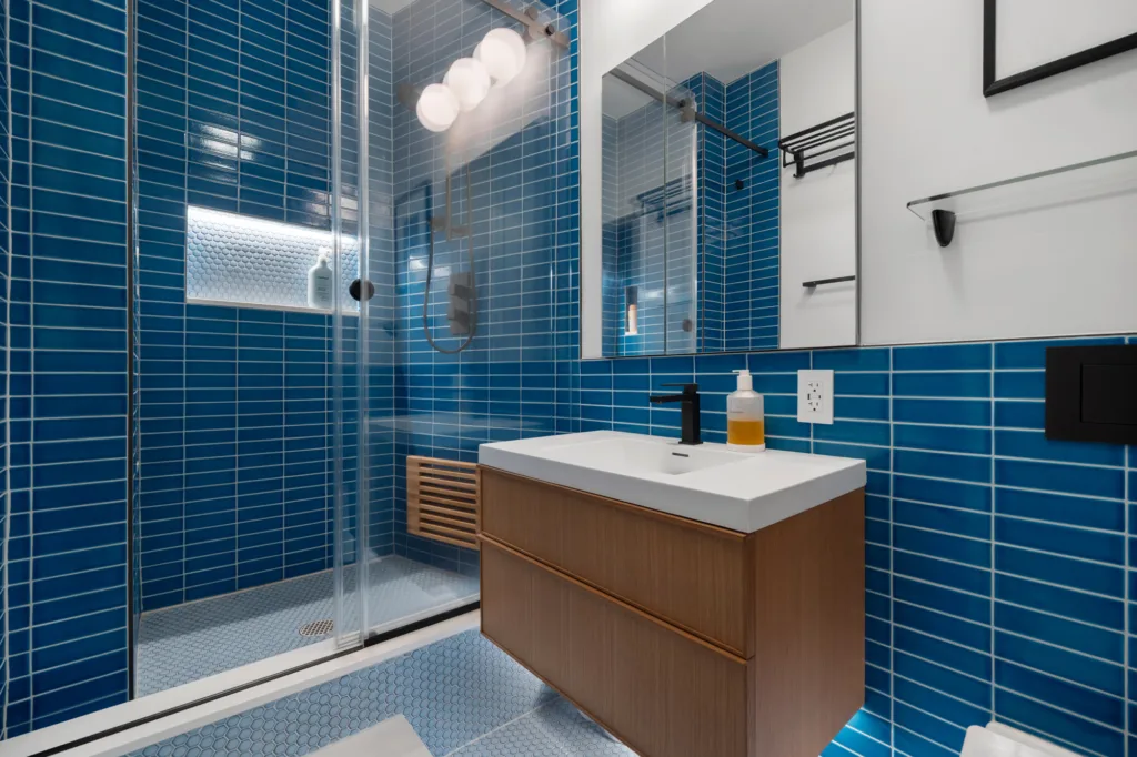 NYC bathroom remodel with blue subway tile, a floating wood vanity, and a glass-enclosed shower
