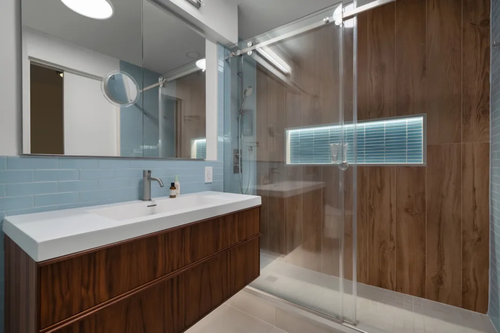 NYC bathroom remodel with a wood vanity, glass shower doors, and wood-look shower wall tile