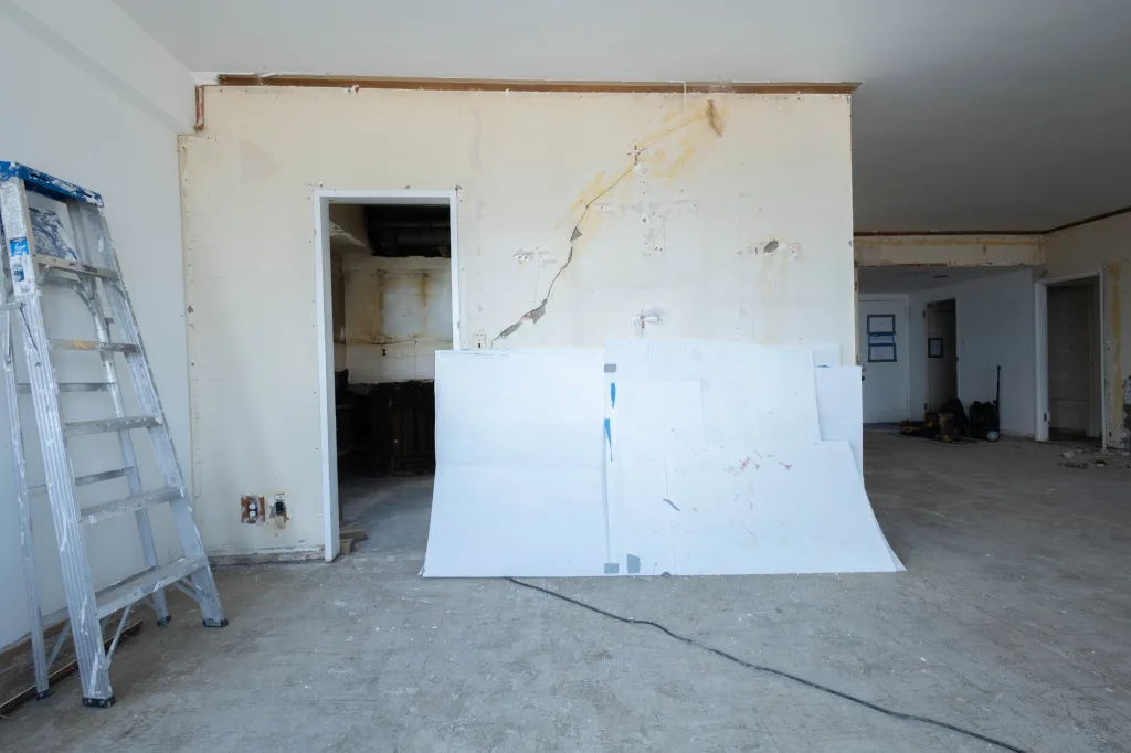 Kitchen before wall removal, with an existing partition, stripped wall finishes, and exposed concrete flooring.
