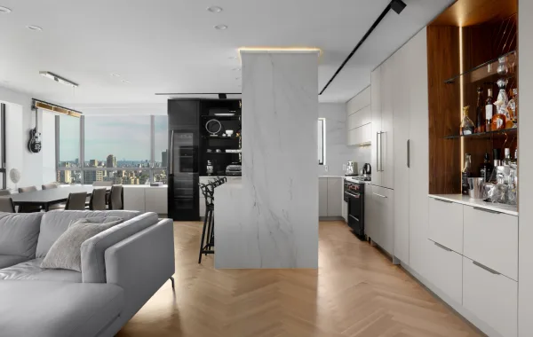 Open-plan kitchen remodeled by NYKB with white cabinetry, an illuminated wood bar, and herringbone wood flooring.