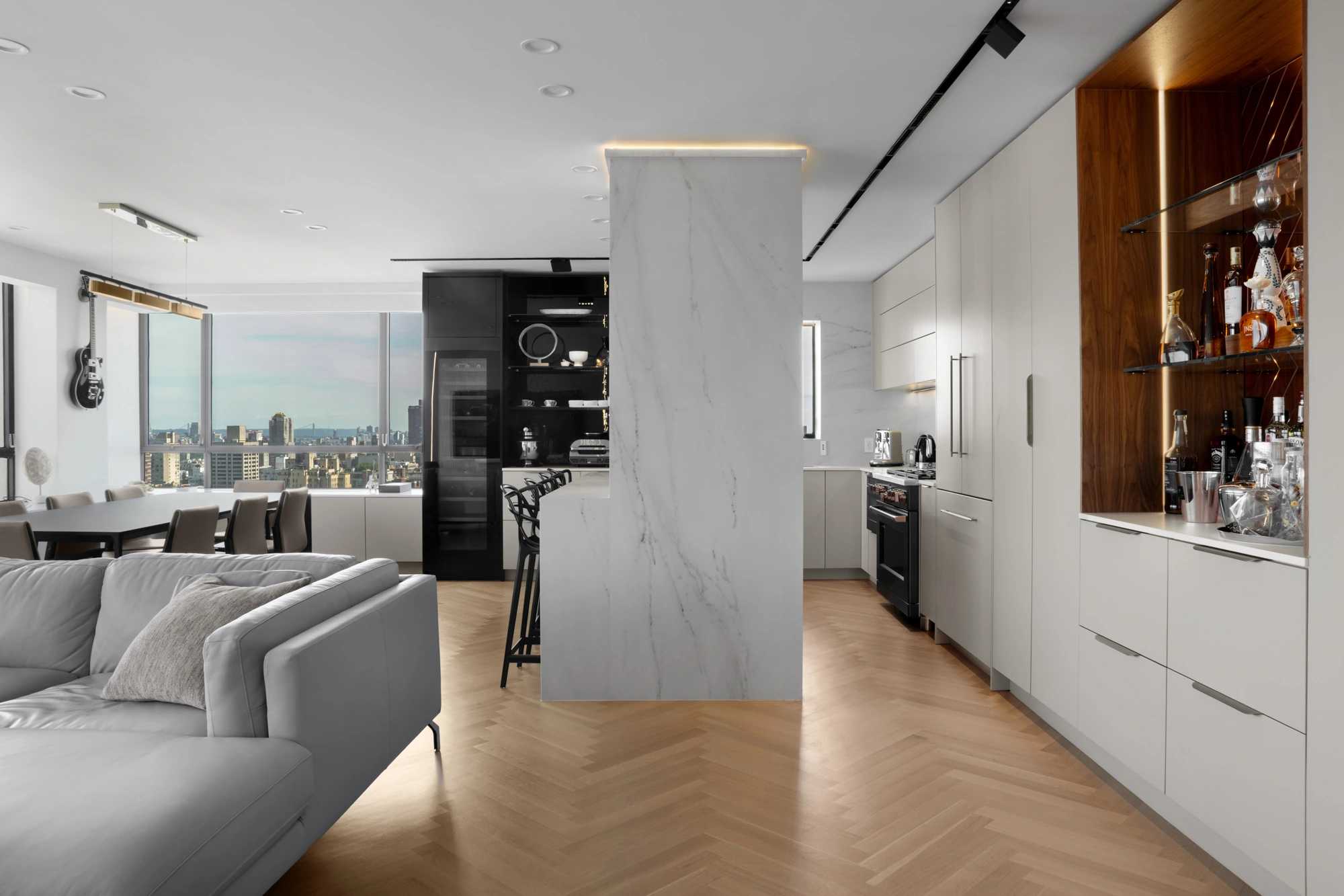 Open-plan kitchen remodeled by NYKB with white cabinetry, an illuminated wood bar, and herringbone wood flooring.